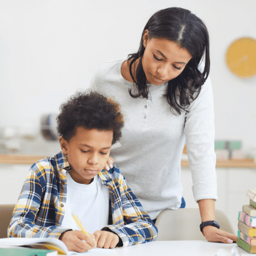 African American mom standing over her son doing homeschooling at the table